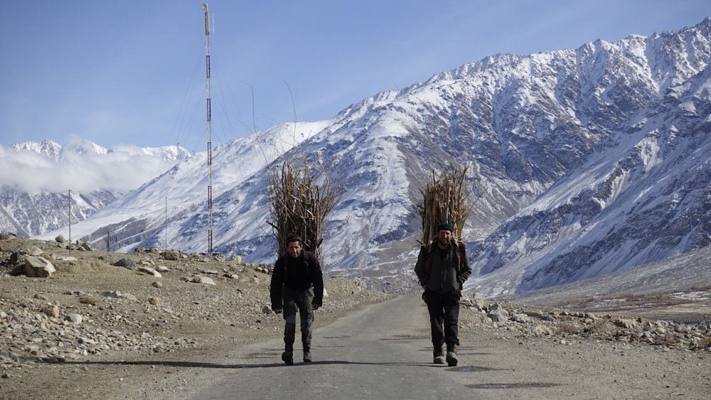 two people walking down a dirt road with trees on their heads