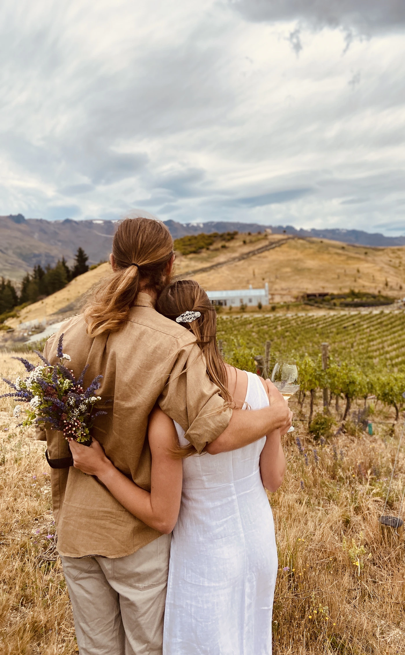 Couple in wedding attire among the rows of a hillside vineyard