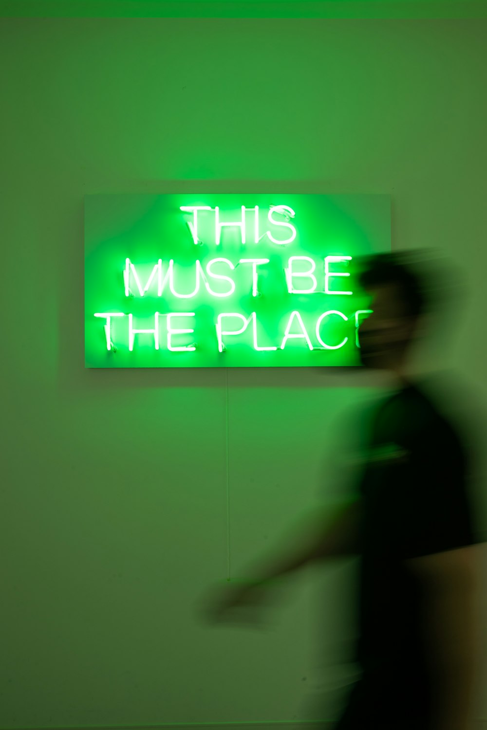 a man walking past a neon sign that says, this must be the place