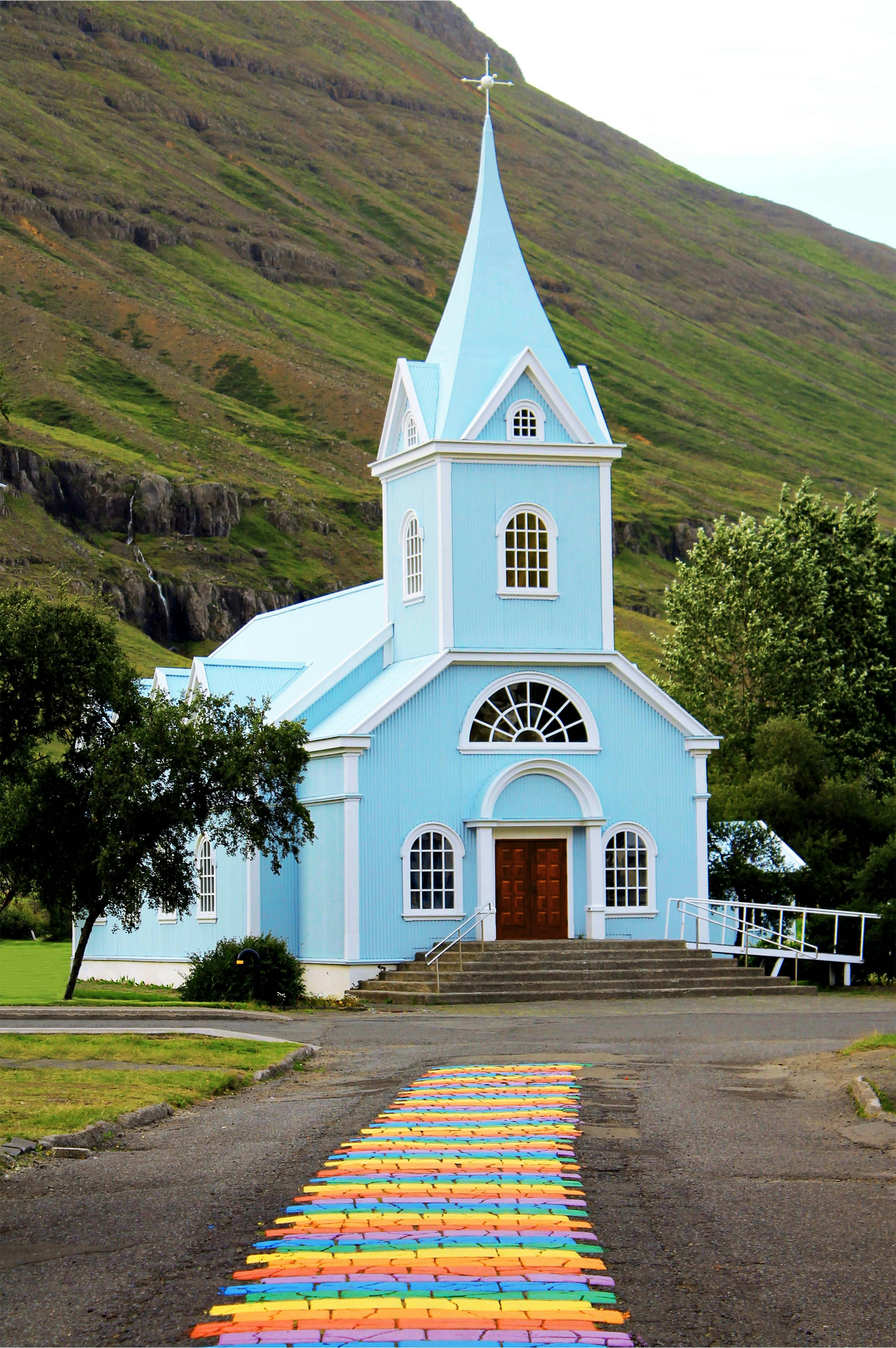 Una pequeña iglesia azul con un campanario en una colina