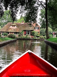 a red boat traveling down a river next to a house
