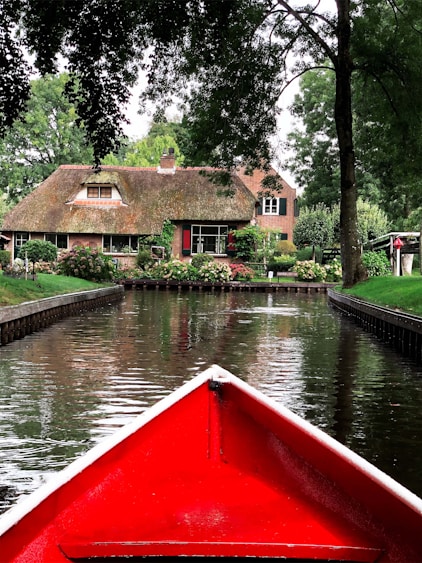 a red boat traveling down a river next to a house