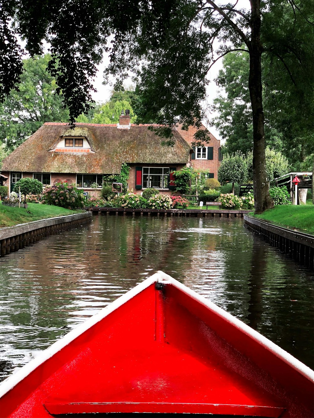 a red boat traveling down a river next to a house