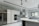 A modern kitchen featuring sleek, white cabinetry and marble-patterned walls. There's a double-door stainless steel refrigerator, an integrated oven, and a microwave. The kitchen island has a smooth, curved design with hanging pendant lights above it. A large window provides natural light, and there's a stainless steel sink with a modern faucet.