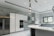 A modern kitchen featuring sleek, white cabinetry and marble-patterned walls. There's a double-door stainless steel refrigerator, an integrated oven, and a microwave. The kitchen island has a smooth, curved design with hanging pendant lights above it. A large window provides natural light, and there's a stainless steel sink with a modern faucet.