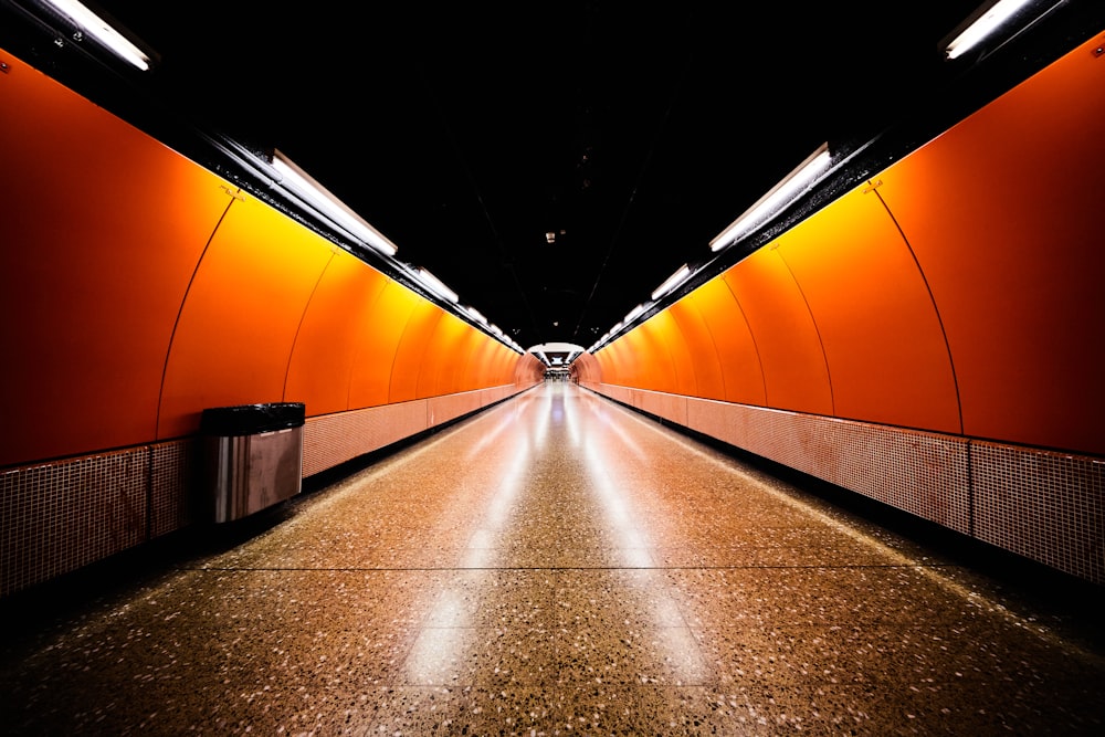 a long tunnel with orange walls and a trash can