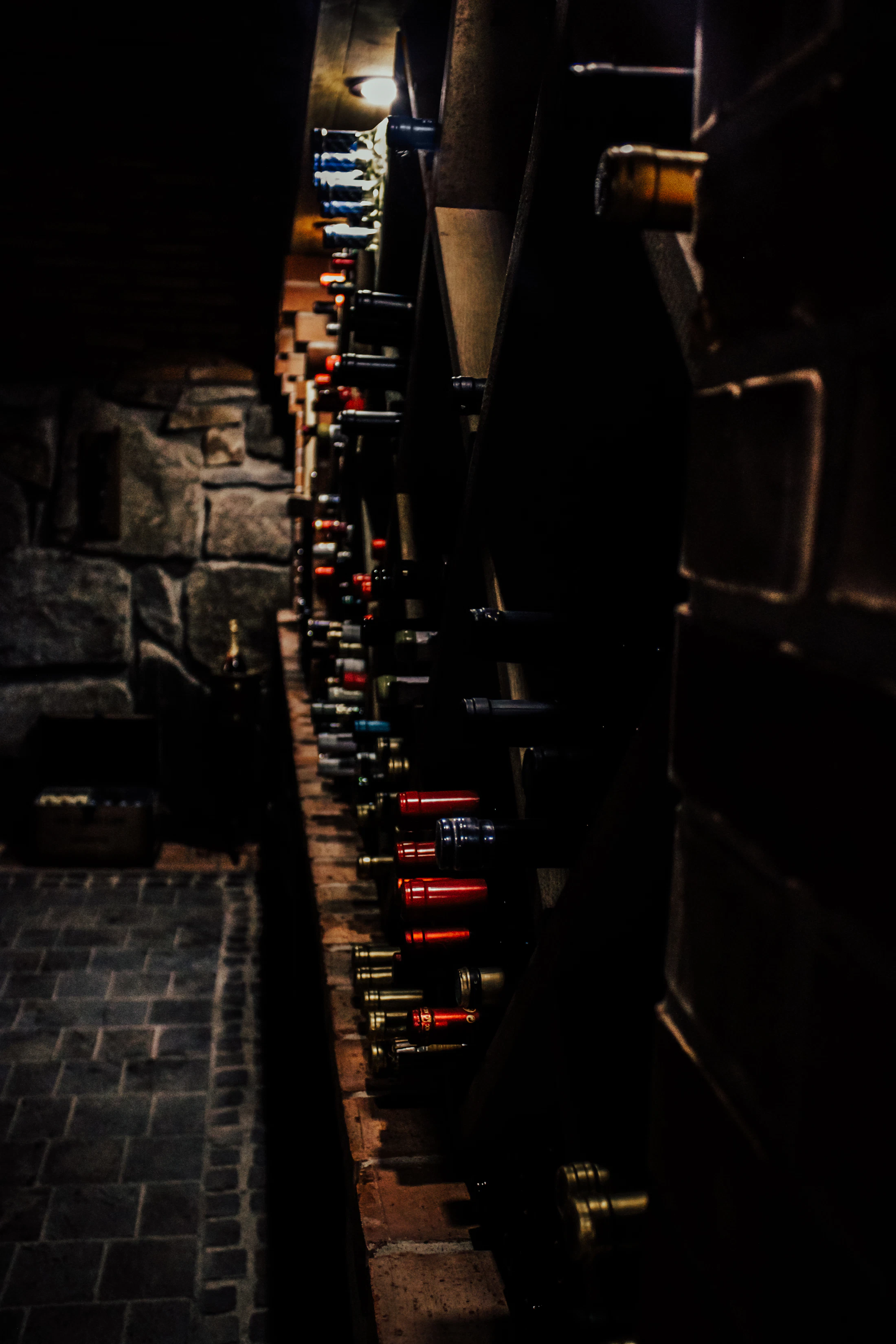 Bottles resting in a stone wine cellar, lit by one lamp