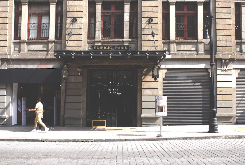 a man walking down a street past a tall building