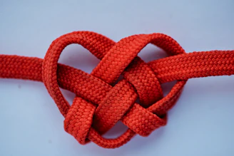 Minimalist heart-shaped knot made of red thread on a clean white background.