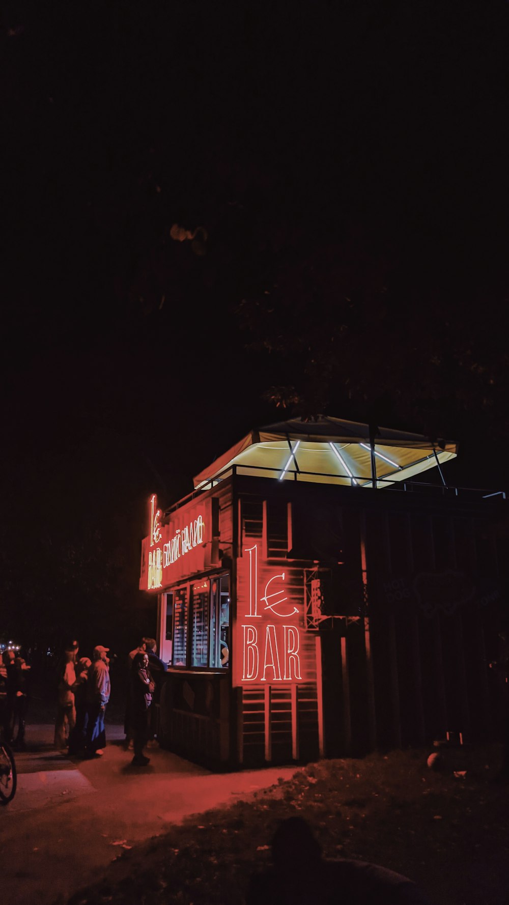 Un bar iluminado por la noche con gente parada alrededor