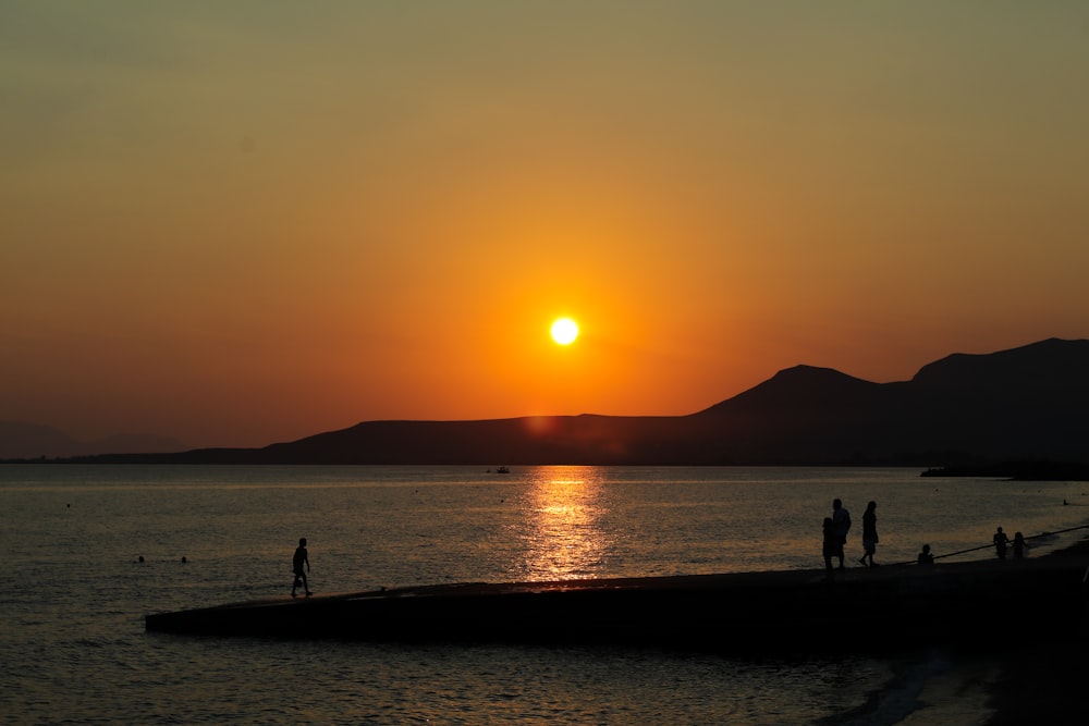 a group of people standing on top of a beach under a sunset