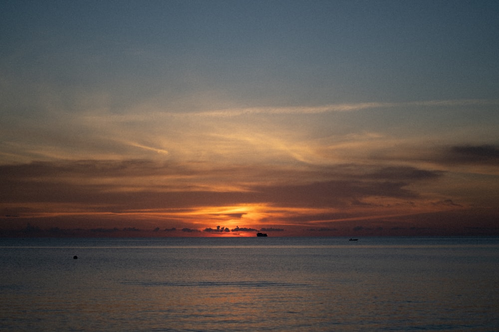 the sun is setting over the ocean on a cloudy day