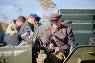 A group portrait of veterans in uniform, standing proudly in front of their military vehicle.