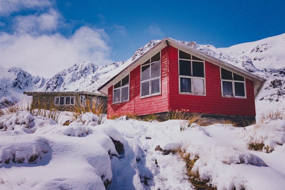 a red house in the snow with mountains in the background