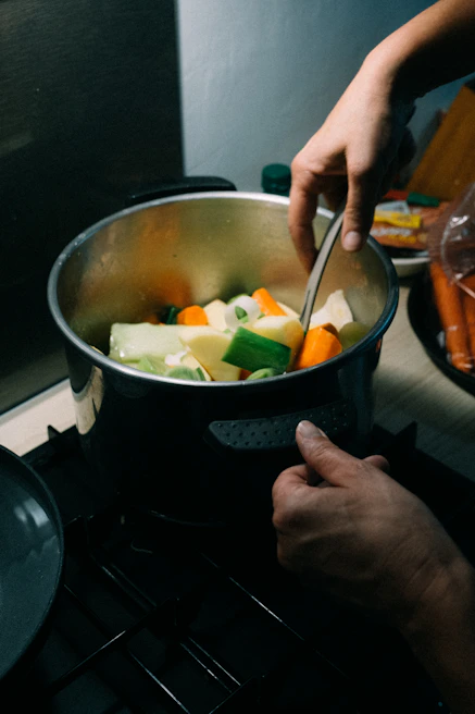 Warm kitchen scene with hands gently stirring a pot of colorful vegetable stew, sunlight streaming through a window