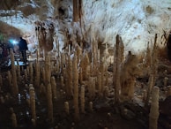 Travelers exploring the mysterious limestone formations inside a cave, their headlamps casting warm glows.