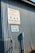 A corrugated metal wall with two signs attached. The top sign reads 'Community Compost Company' with a phone number and website. Below it, another sign indicates 'Office' with an arrow pointing right.
