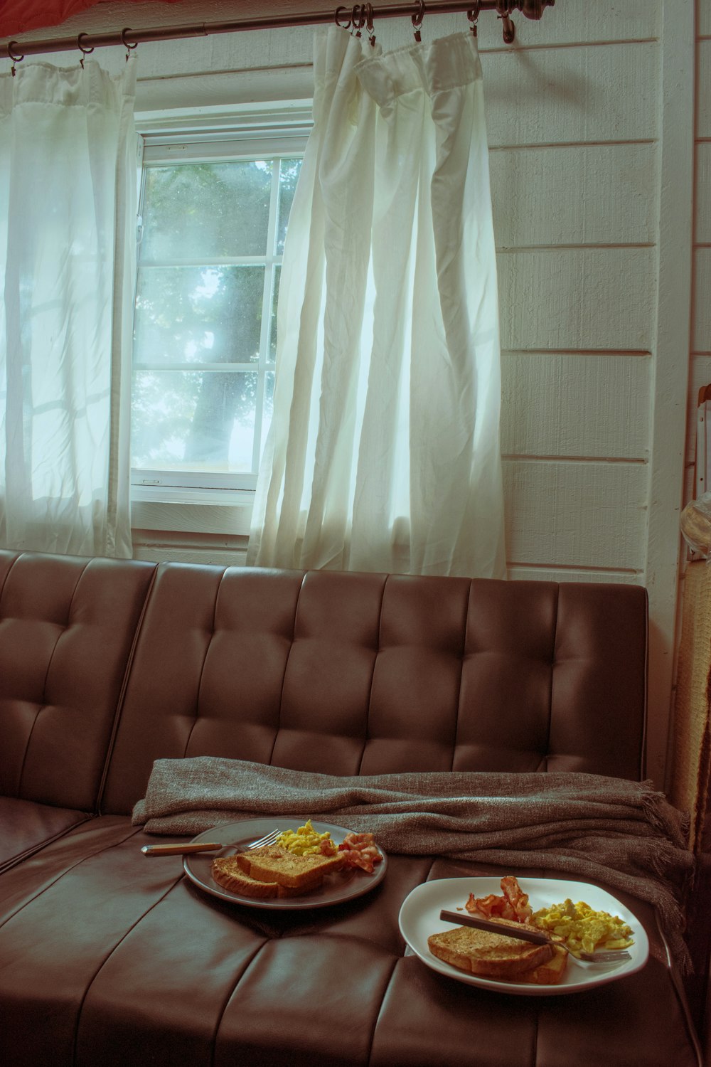 two plates of food sit on a couch in front of a window