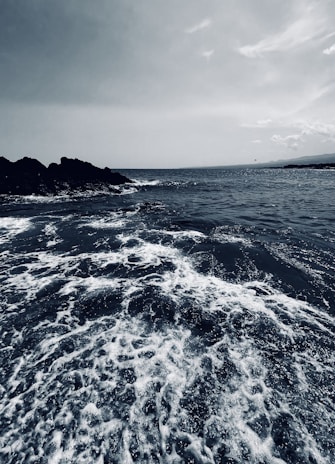 Monochrome image of a rugged coastline with crashing waves and dramatic clouds overhead.