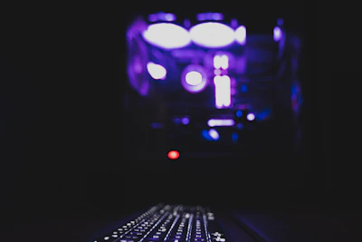 Close-up of a keyboard and mouse setup with a glowing monitor in the background.
