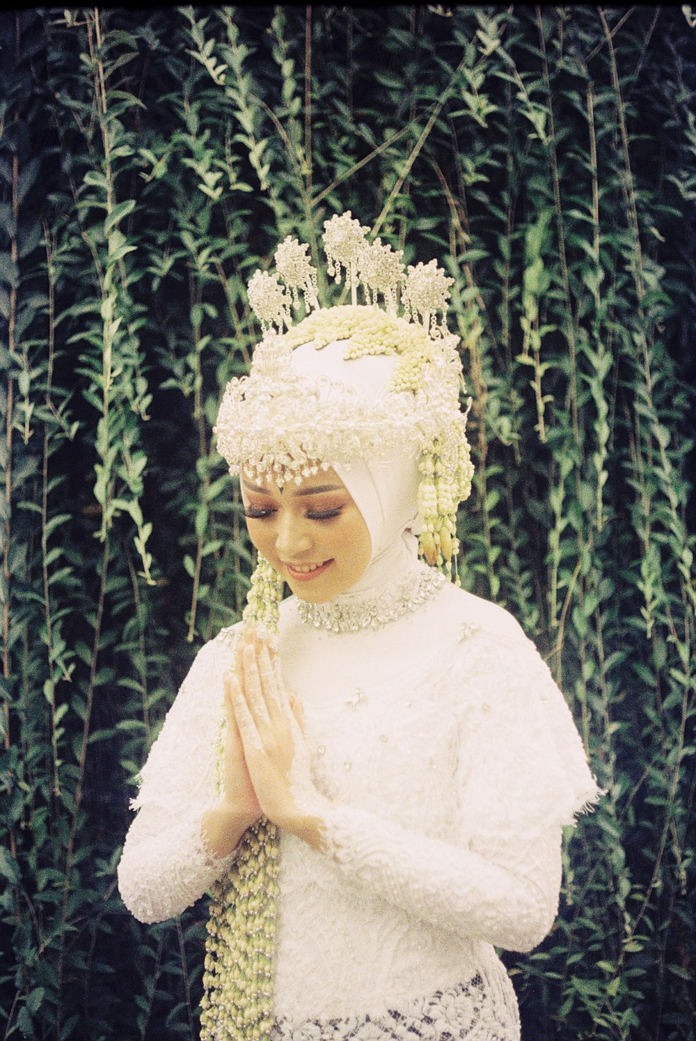 a woman in a white dress standing in front of a bush