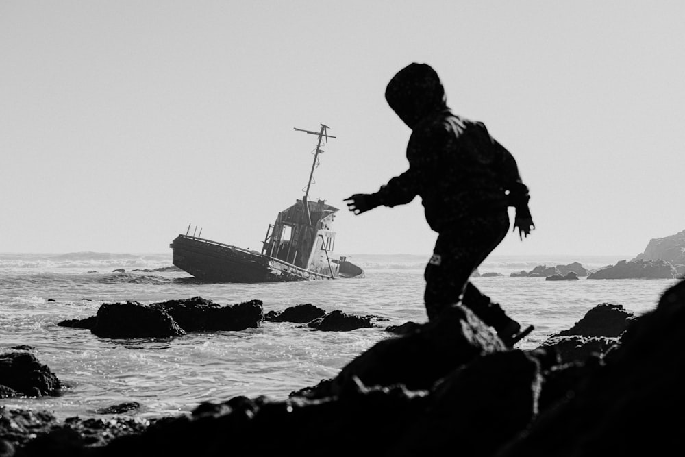 a person standing on rocks near a boat in the ocean