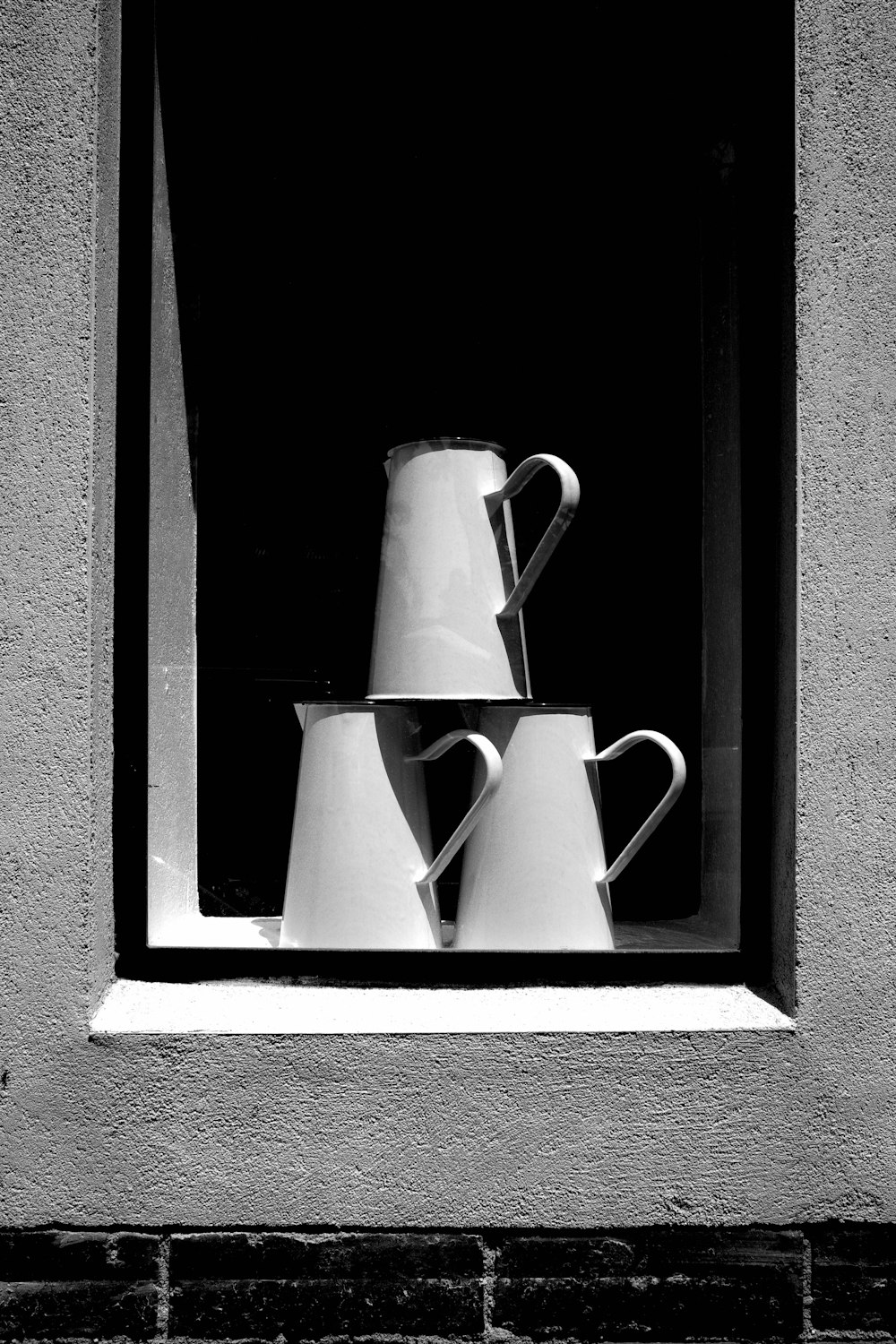 a black and white photo of a window with three coffee cups
