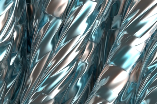 A close-up view of twisted, metallic surfaces with a smooth, reflective texture. The surfaces have an intricate pattern, featuring shiny blue and silver hues that create a futuristic and abstract visual effect.