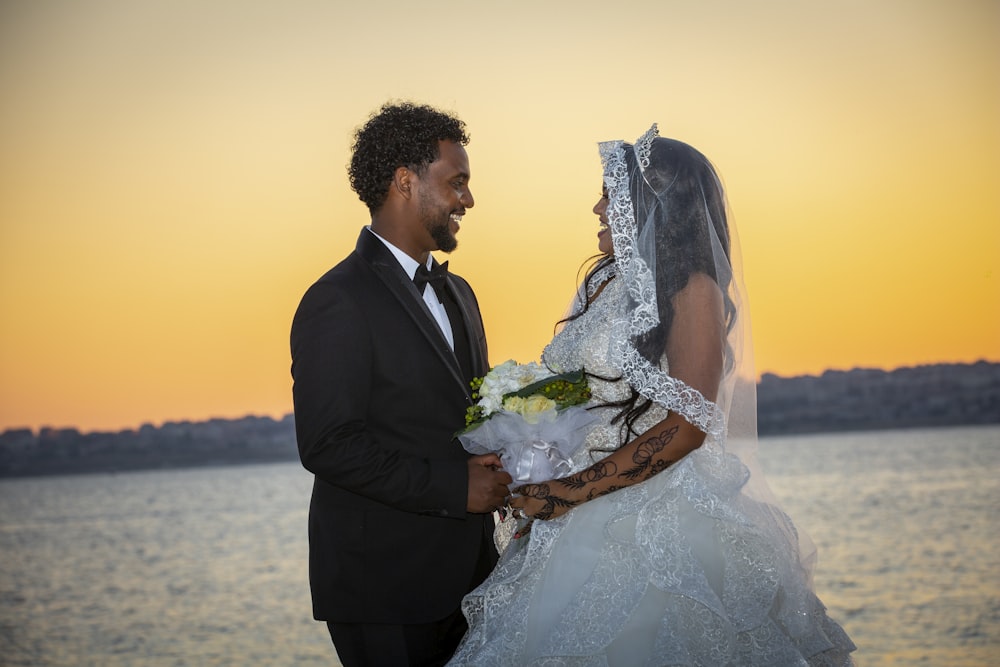 a bride and groom standing next to each other in front of a body of water