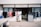 A small shop with an open entrance displaying a variety of clothing items outside. Brightly colored shirts and dresses hang on racks, while other clothes are visible through the shop's doorway. The shop front is simple, with a sign above the door and a concrete sidewalk in front.
