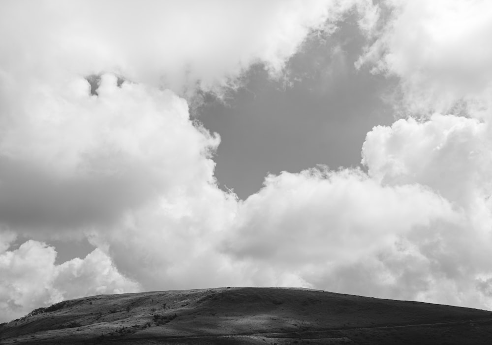 a black and white photo of clouds over a hill