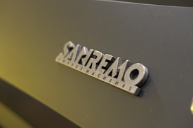 Close-up view of a 'Sanremo Coffee Machines' logo on a dark surface.