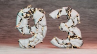 Two large numbers, nine and three, appear to be made of stone with glowing fissures running through them, creating a striking visual effect. The surface is rough, and the contrasting bright orange and black colors highlight the cracks, against a muted background.
