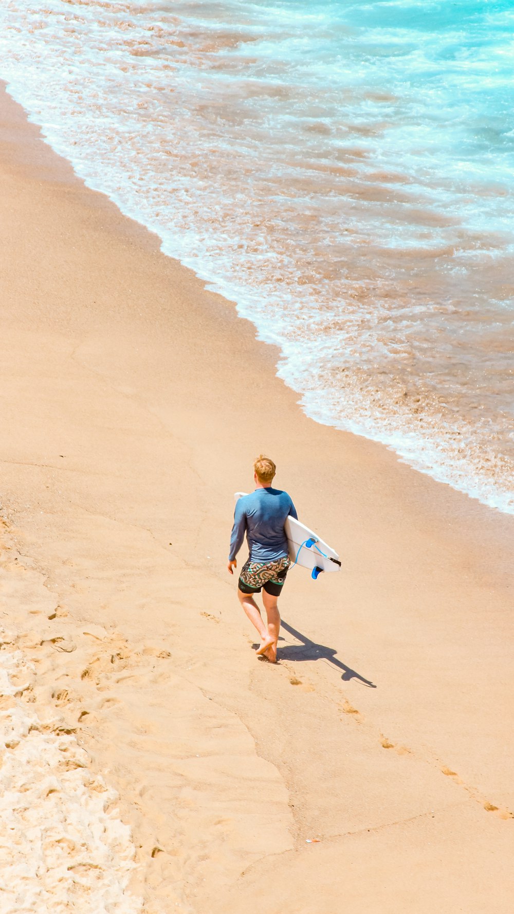a man walking down a beach holding a surfboard