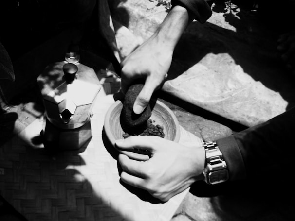Close-up of hands grinding fresh spices in a traditional stone mortar.