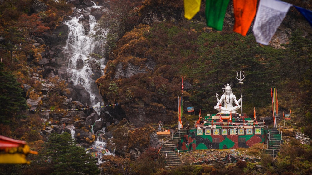 a large white statue sitting in front of a waterfall