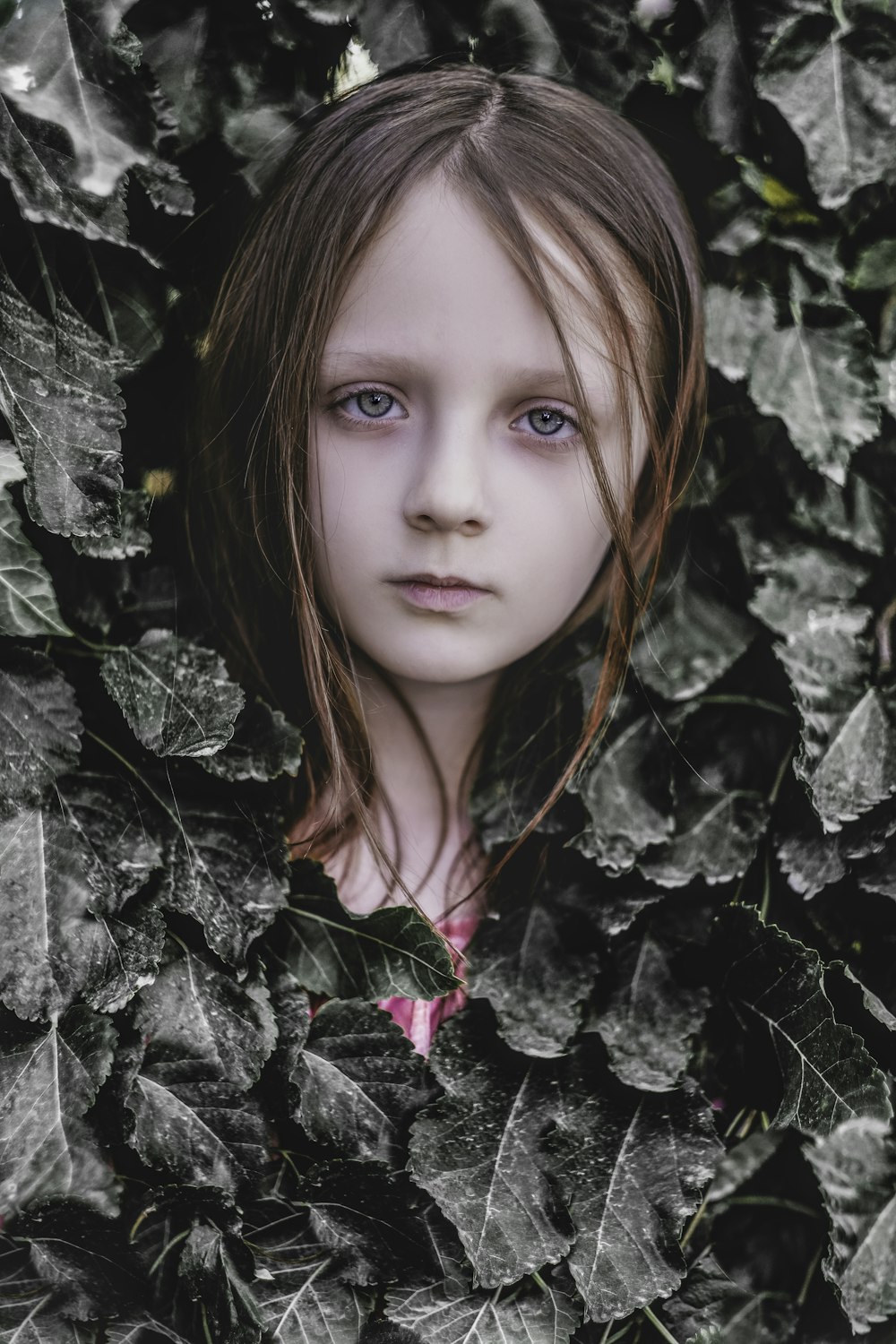 a young girl with blue eyes is surrounded by leaves
