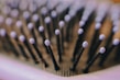 Close-up of a hairbrush with black bristles tipped with light purple rounded ends. The image is focused on the bristles, creating a pattern across the frame, with a soft background blur.