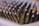 Close-up of a hairbrush with black bristles tipped with light purple rounded ends. The image is focused on the bristles, creating a pattern across the frame, with a soft background blur.