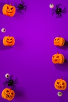 A vibrant purple background is adorned with scattered Halloween-themed items along the edges, including carved pumpkins with various facial expressions, artificial spiders, and plastic eyeballs, creating a playful and spooky arrangement.