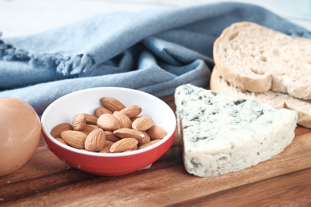 a bowl of almonds, bread, and an egg on a cutting board