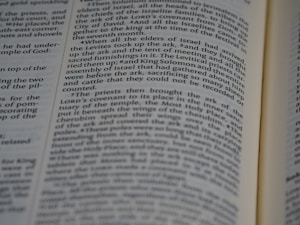 A close-up view of an open book with black text on white pages. The text is aligned in columns and features a narrative style, likely from a religious or historical context.