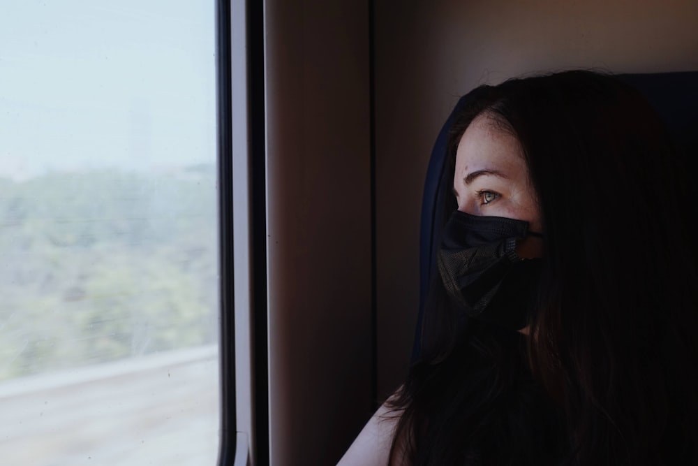 a woman wearing a face mask looking out a train window