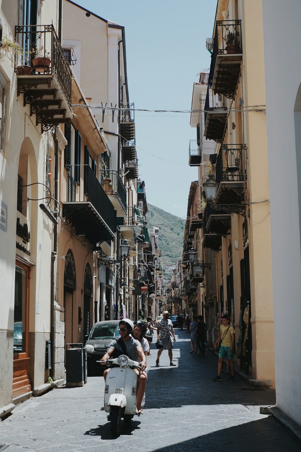 a couple of people riding a scooter down a street