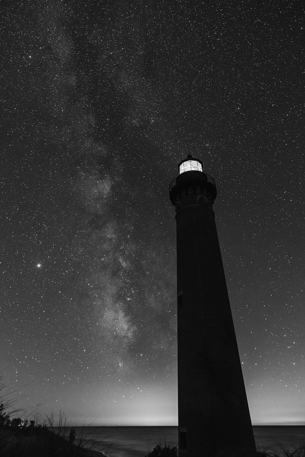 a black and white photo of a lighthouse under the stars