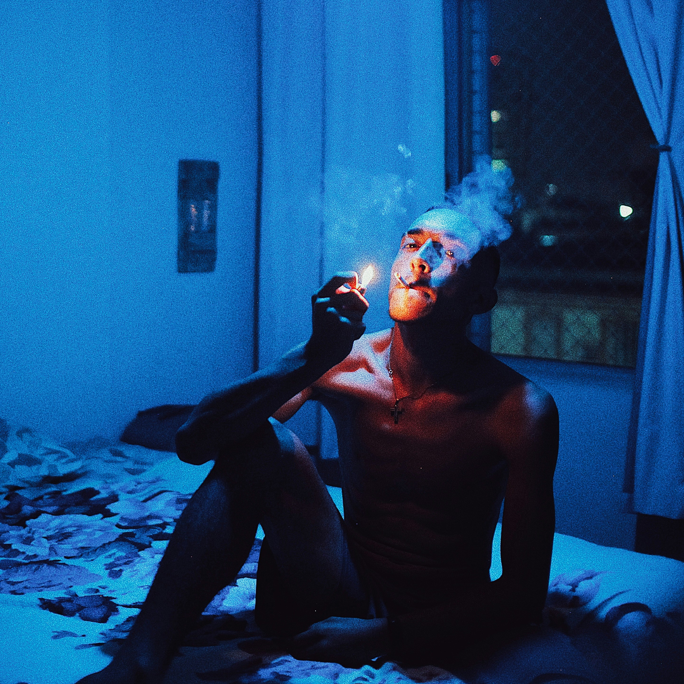 a man sitting on a bed smoking a cigarette