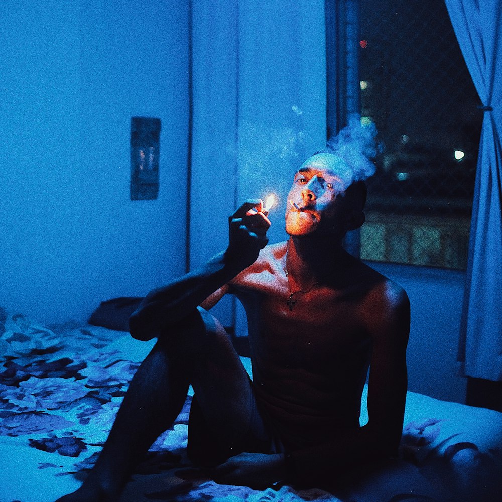 a man sitting on a bed smoking a cigarette