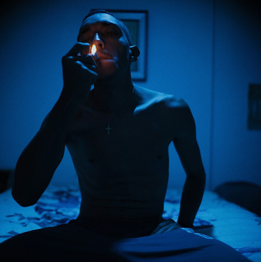 a man sitting on a bed smoking a cigarette