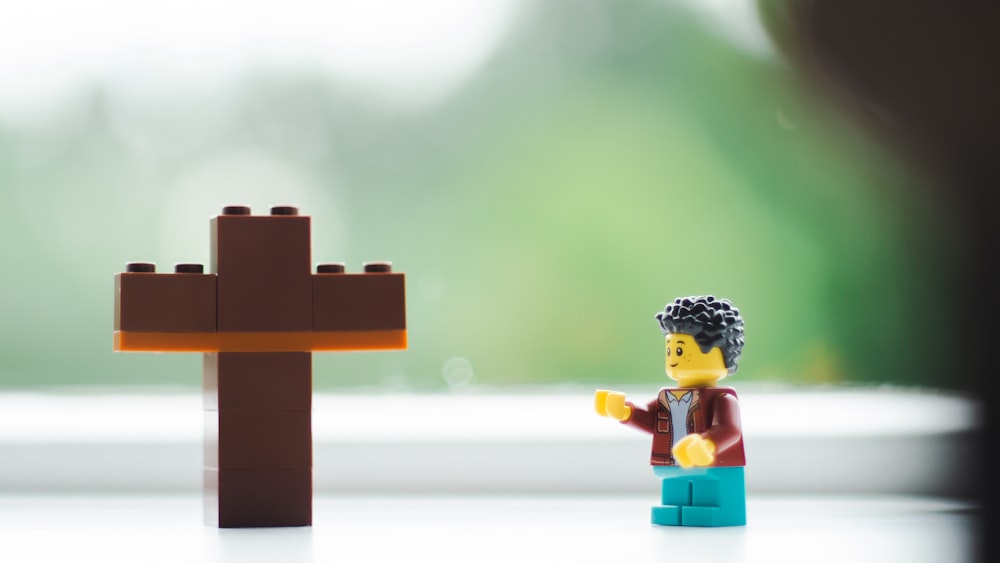 a lego man standing next to a wooden cross