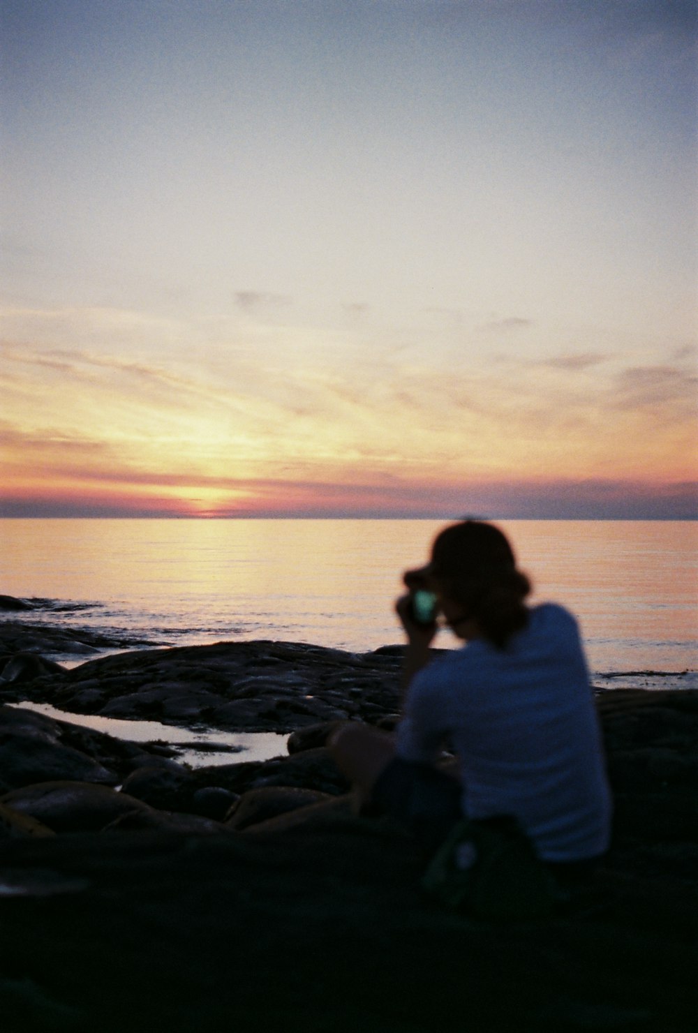a person sitting on a beach taking a picture of the sunset